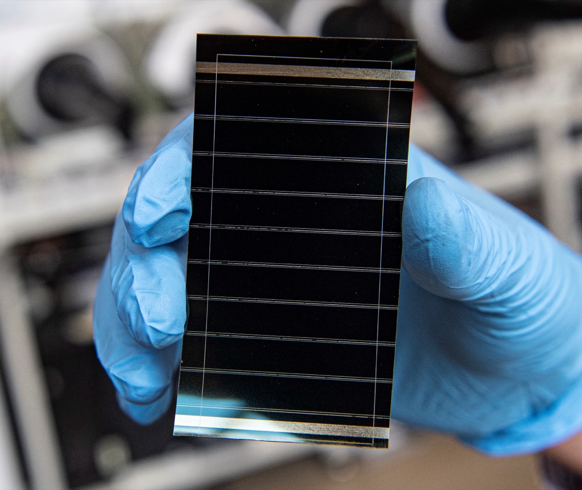 A gloved hand holding a thin, flexible perovskite solar cell module, illustrating the perovskite layer used in JinkoSolar's record-setting 34.82% perovskite-on-silicon tandem cell