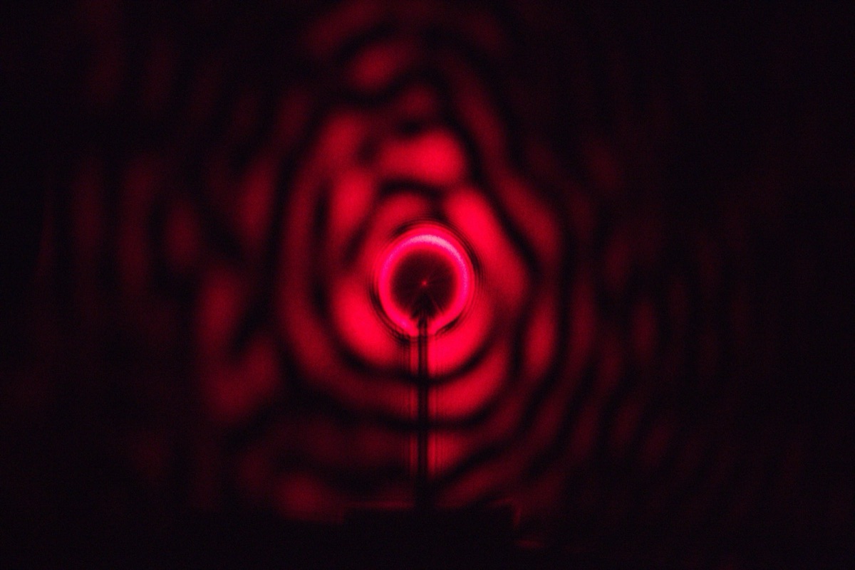 A red laser passing a small spherical obstacle produces a bright Poisson (Arago) spot at the center of its circular shadow — the 200-year-old diffraction phenomenon NTU Singapore scientists used to generate optical skyrmions.